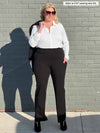 Miik model Jillian (five feet ten, xxlarge) smiling in front of a brick wall wearing Miik's Sierra high waisted pocket pant in black with a collared shirt in white and sunglasses 