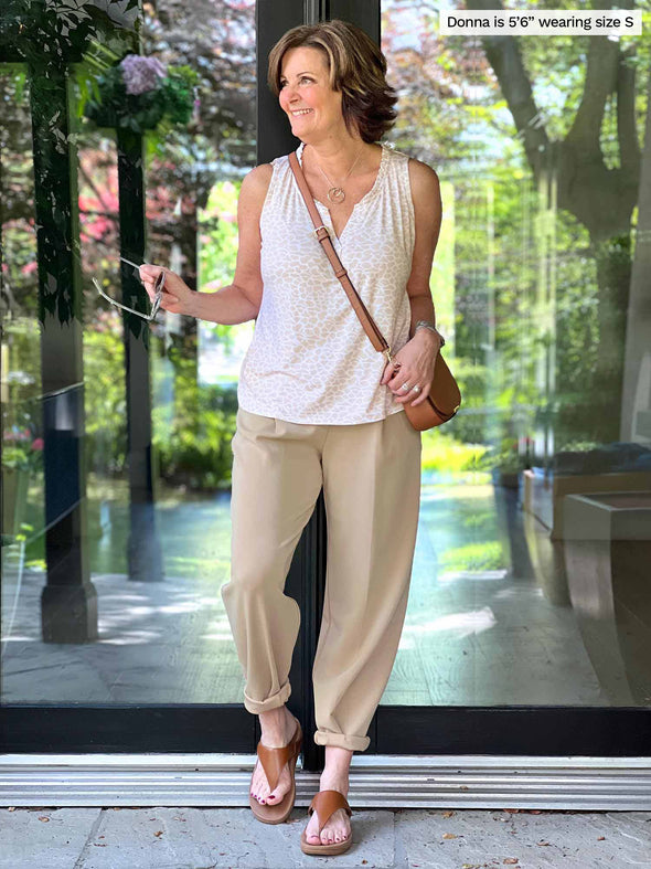 Miik founder Donna (five feet six, small) standing in front of a doorway and looking away wearing Miik's Skye ruffle neck blouse in cobblestone print with a scuba pant in wheat and a crossbody purse 