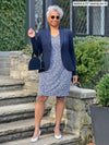 Woman standing in front of a house wearing Miik's Sofia reversible everyday dress in blue ditsy print under a navy blazer.