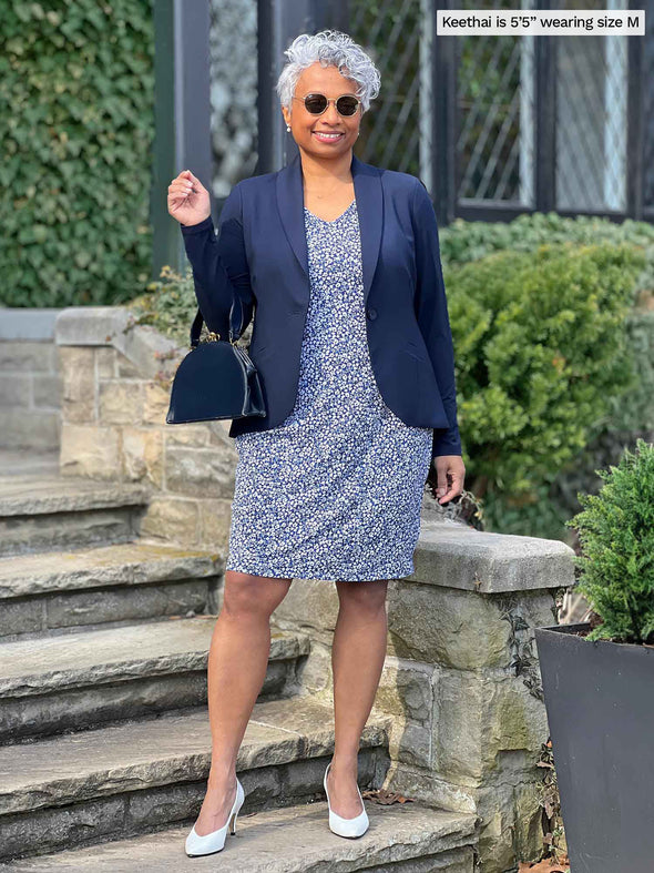 Woman standing in front of a house wearing Miik's Sofia reversible everyday dress in blue ditsy flower print with a navy blazer.