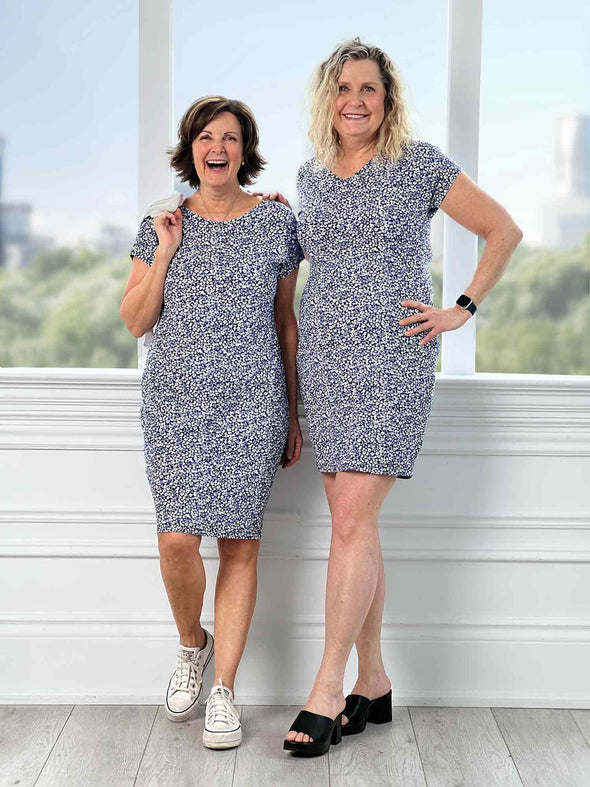 Two women standing in front of a window wearing Miik's Sofia reversible everyday dress in blue ditsy print.