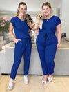 Miik models Jo and Bri standing next to each other both holding a puppy and wearing the same jumpsuit: Miik's Stef v-neck open-back capri jumpsuit in ink blue