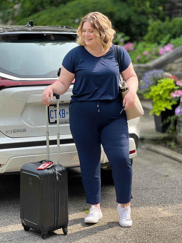 Miik model Bri (size XL, 5 foot 5) wearing the Stef open-back jumpsuit as she gets ready to put a travel suitcase in her car for a trip.