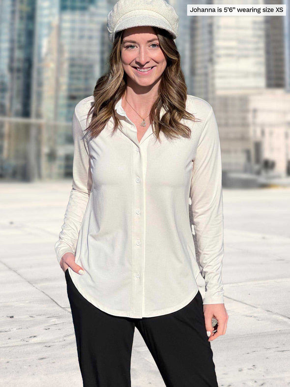 Miik model Johanna (5’6”, xsmall) smiling with one hand on pockets wearing Miik's Susan button up dress shirt in natural along with a black jogger