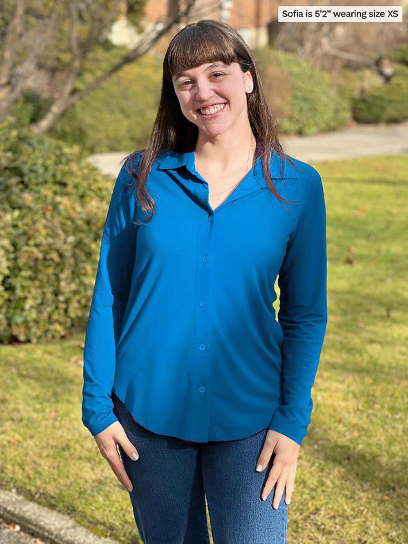 Miik model Sofia (5'2", xsmall) smiling wearing Miik's Susan button up dress shirt in peacock blue with jeans 