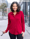 Miik model Meron (5'3", xsmall) smiling wearing Miik's Susan button up dress shirt in red wine with a black pant