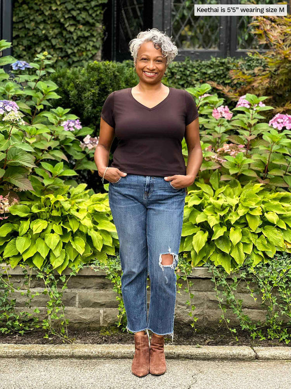 Miik model Keethai (5'5", medium) smiling with hand on pockets wearing a ripped jeans along with Miik's Sutton v-neck classic tee in dark chocolate brown