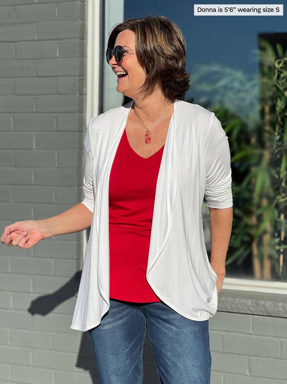 Miik founder Donna (5'5", small) smiling and looking away wearing Miik's Sutton v-neck classic tee in poppy red along with a white waterfall cardigan and jeans 