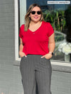 Miik model Christal (5'3", large) smiling and looking away wearing Miik's Sutton v-neck classic tee in poppy red along with a pinstripe charcoal pant and sunglasses 