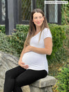 Miik model Jo (5'6", xsmall) pregnant sitting on a backyard wearing Miik's Sutton v-neck classic tee in white and black legging
