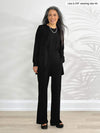 Miik model Lisa (5'6", xsmall) smiling while standing in front of a white wall wearing an all black outfit: Miik's Teanna scoop neck tank top, Reed wide leg and Sade cardigan