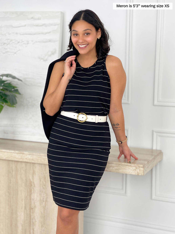 Miik model Meron (5'3", xsmall) smiling wearing Miik's Teanna high neck tank top in black wide pinstripe along with a matching stripe skirt and a white belt 