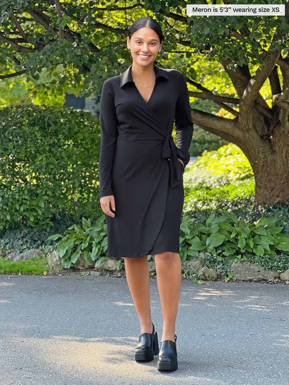 Miik model Meron (5'3", xsmall) smiling wearing Miik's Tierney collared faux wrap dress in black