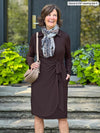 Miik founder Donna (5'6", small) looking away and smiling wearing Miik's Tierney collared faux wrap dress in dark chocolate with a animal print brown scarf and a shoulder bag