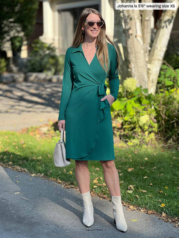 Miik model Johanna (5'6", xsmall) looking away with hands on pockets wearing Miik's Tierney collared faux wrap dress in jade melange, sunglasses and boots