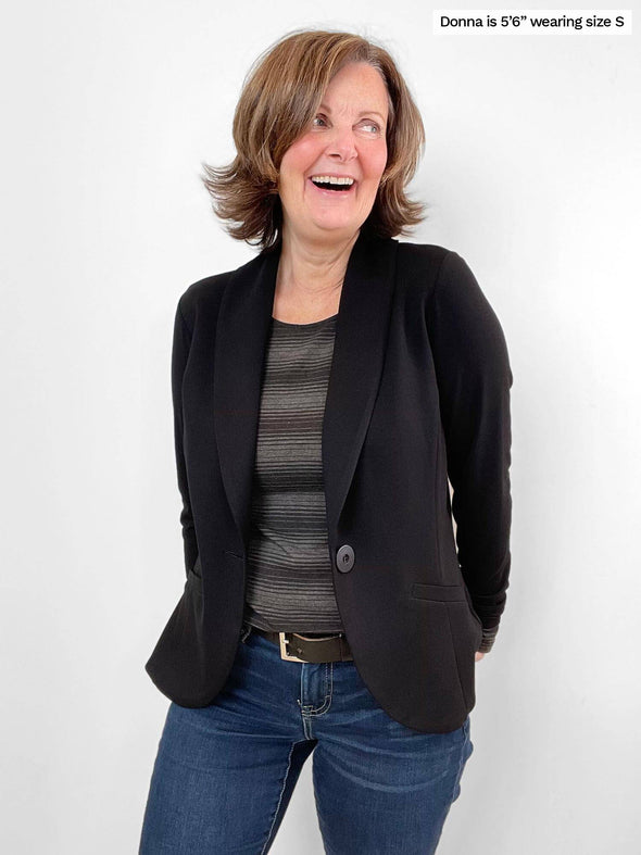 Woman standing in front of a white wall wearing Miik's Tray long sleeve striped tee in charcoal stripe with jeans and a blazer.