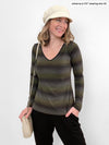 Woman standing in front of a white wall wearing Miik's Tray long sleeve striped tee in green stripe with black pants.
