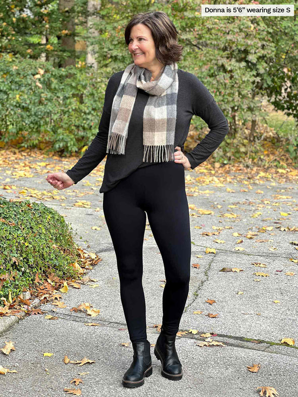 Miik founder Donna (5'3", small) smiling and looking away wearing Miik's Tyson mid-rise fleece legging in black with a charcoal long sleeve top and a neutral scarf 