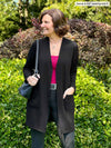 Miik founder Donna (5'6", small) smiling and looking away wearing Miik's Vula belted cardigan with pockets in black with a charcoal pant, belt and a bordeaux tank top
