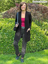 Miik founder Donna (5'6", small) smiling wearing Miik's Vula belted cardigan with pockets in black with a charcoal pant, belt and a bordeaux tank top 