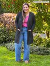 Miik model Christal (5'3", large) smiling wearing jeans and a pink top along with Miik's Vula belted cardigan with pockets in charcoal
