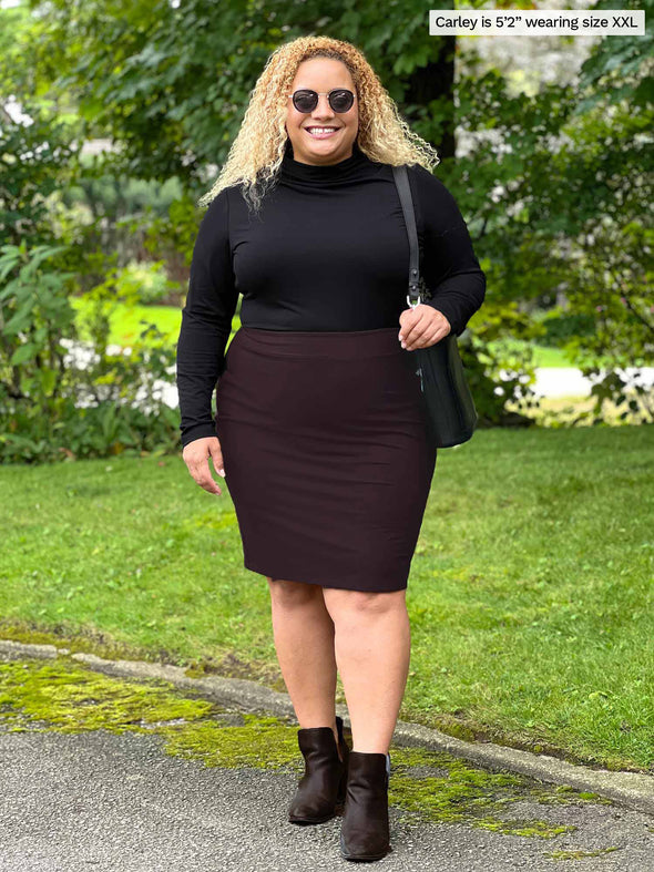 Miik model Carley (five feet two, xxlarge) smiling wearing Miik's Wallace long sleeve draped blouse in black with a skirt in dark chocolate 