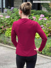 Miik model Johanna (five feet six, size xsmall) standing with her back towards the camera showing the back of Miik's Wallace long sleeve draped blouse in bordeaux