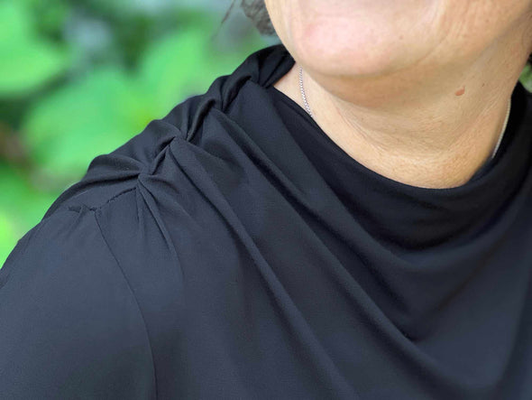 A close up image of the draped detail of Miik's Wallace long sleeve draped blouse in black