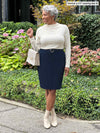 Miik model Keethai (five feet five, medium) smiling and looking away wearing a pencil skirt in navy, belt and Miik's Wallace long sleeve draped blouse in natural with a purse and boots in the same colour 