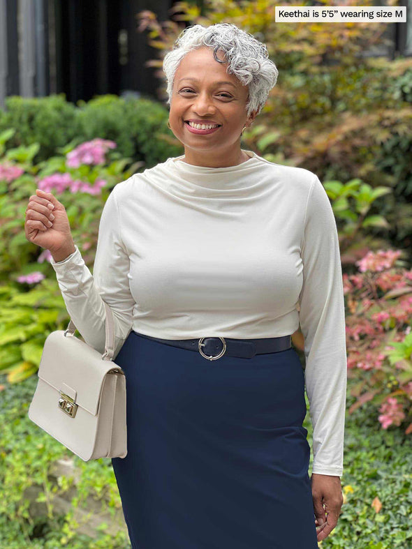 Miik model Keethai (five feet five, medium) smiling wearing Miik's Wallace long sleeve draped blouse in natural with a pencil skirt in navy and a belt