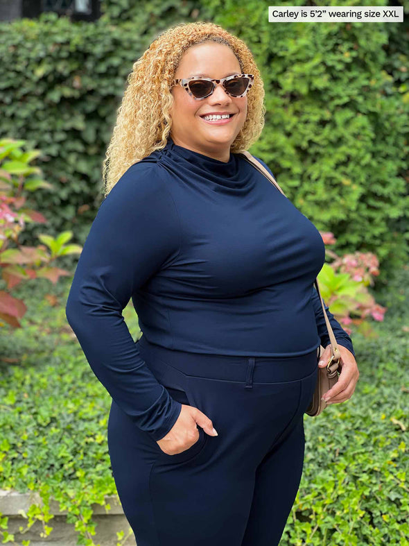 Miik model Carley (five feet two, xxlarge) smiling while standing sideway wearing an all navy outfit: Miik's Wallace long sleeve draped blouse and Asia pant 