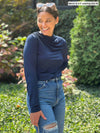 Miik model Meron (five feet three, xsmall) smiling and looking away wearing Miik's Wallace long sleeve draped blouse in navy with jeans