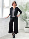 Miik founder Donna (5'6", small) standing next to a window wearing a black flare pant, black and white striped top and Miik's Wesley cropped cardigan in black 