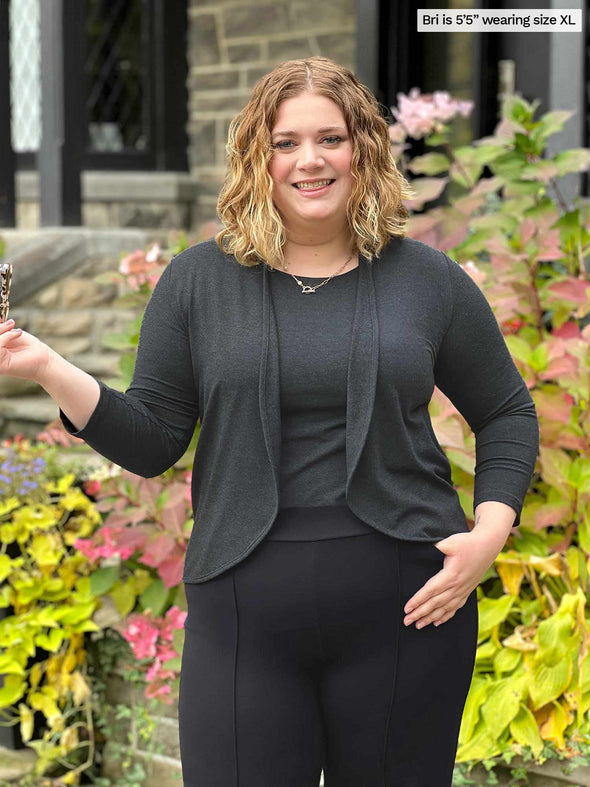 Miik model Bri (5'5", xlarge) smiling wearing Miik's Wesley cropped cardigan in charcoal along with a tank top in the same colour and a black pant