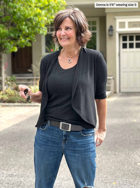 Miik founder Donna (5'6", small) looking away and smiling wearing Miik's Wesley cropped cardigan in charcoal with a tank in the same colour, jeans and a black belt