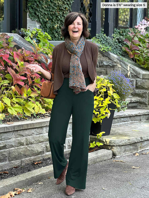 Miik founder Donna (5'6", small) smiling wearing a green pine flare pant with Miik's Wesley cropped cardigan in chocolate melange and a tank top in the same colour. Donna is also wearing a printed scarf 