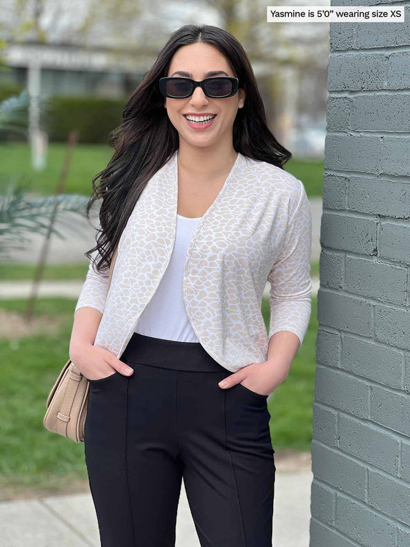 Miik model YAsmine (five feet tall, xsmall, petite) smiling while standing next to a brick wall wearing Miik's Wesley cropped cardigan in cobblestone print with a black pant, white tee and sunglasses 