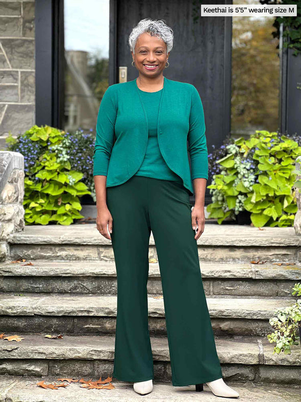 Miik model Keethai (5'5", medium) smiling wearing Miik's Wesley cropped cardigan in jade melange with a tank in the same colour and a flare pant in green pine 