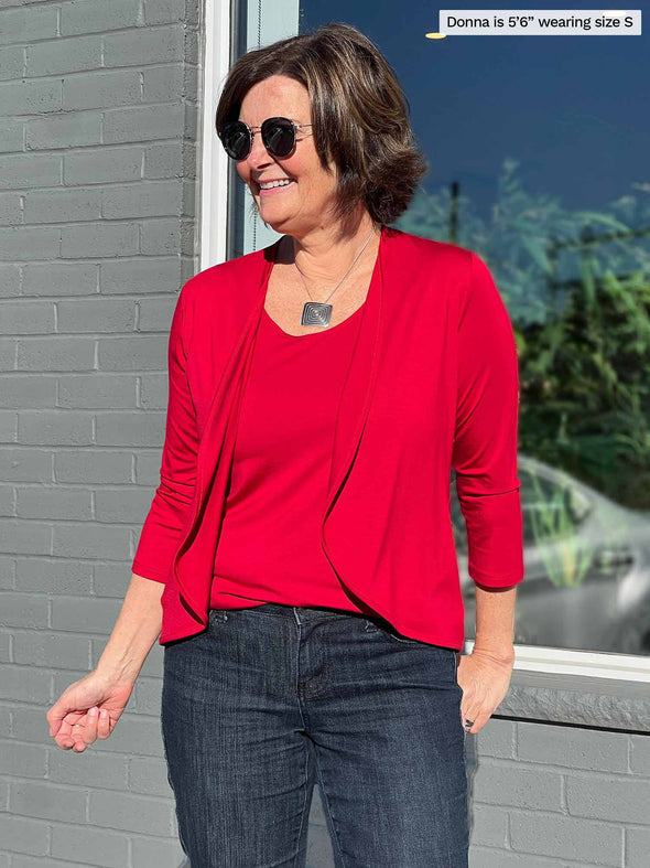 Miik founder Donna (5'6", small) smiling and looking away wearing Miik's Shandra reversible tank top in poppy red along with a cropped cardigan in the same matching colour, jeans and sunglasses 
