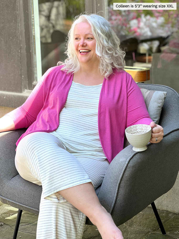 Miik model Colleen (5'3", xxlarge) sitting on a chair smiling wearing a lounge set in grey stripe with Miik's Wesley cropped cardigan in pink 