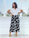 Miik model Meron (5'3", xsmall) smiling while standing in front of a window/white wall wearing a printed capri pant along with Miik's Yasmina band collar blouse in white 