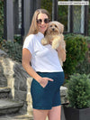Miik model Jo (5'6", small) smiling while standing sideway and holding a puppy wearing Miik's Yasmina band collar blouse in white tucked in a stretch short in teal   