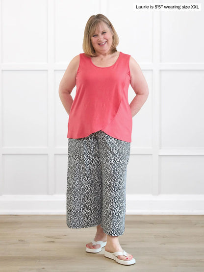 Woman wearing a pink sleeveless top and patterned pants standing against a white wall. 