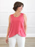Woman wearing a pink sleeveless top and white pants against a white wall. 