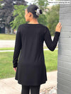 Miik model Meron (five feet three, xsmall) standing with her back towards the camera showing the back of Miik's Zuri long sleeve pocket tunic in black