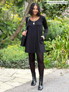 Miik model Meron smiling wearing  Miik's Zuri long sleeve pocket tunic in black as a dress and boots 