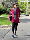 Miik model Meron (five feet three, xsmall) walking with hands on her pockets wearing  Miik's Zuri long sleeve pocket tunic in bordeaux with a black legging and a scarf