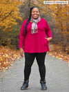 Miik model plus size Kimesha (5'8", size 3x) wearing Miik's Zuri long sleeve pocket tunic in bordeaux with a matching colour printed scarf, black leggings and boots  