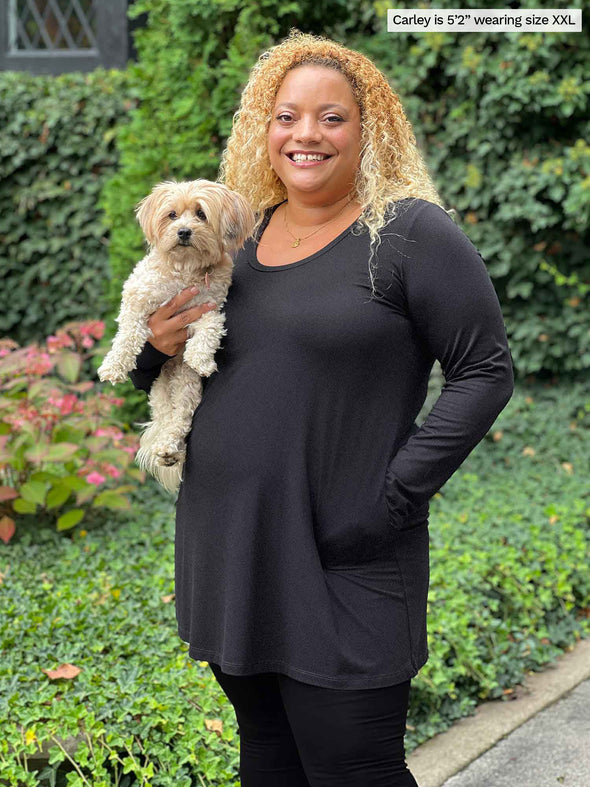 Miik model Carley (five feet two, xxlarge) smiling while holding a puppy wearing  Miik's Zuri long sleeve pocket tunic in charcoal with leggings 