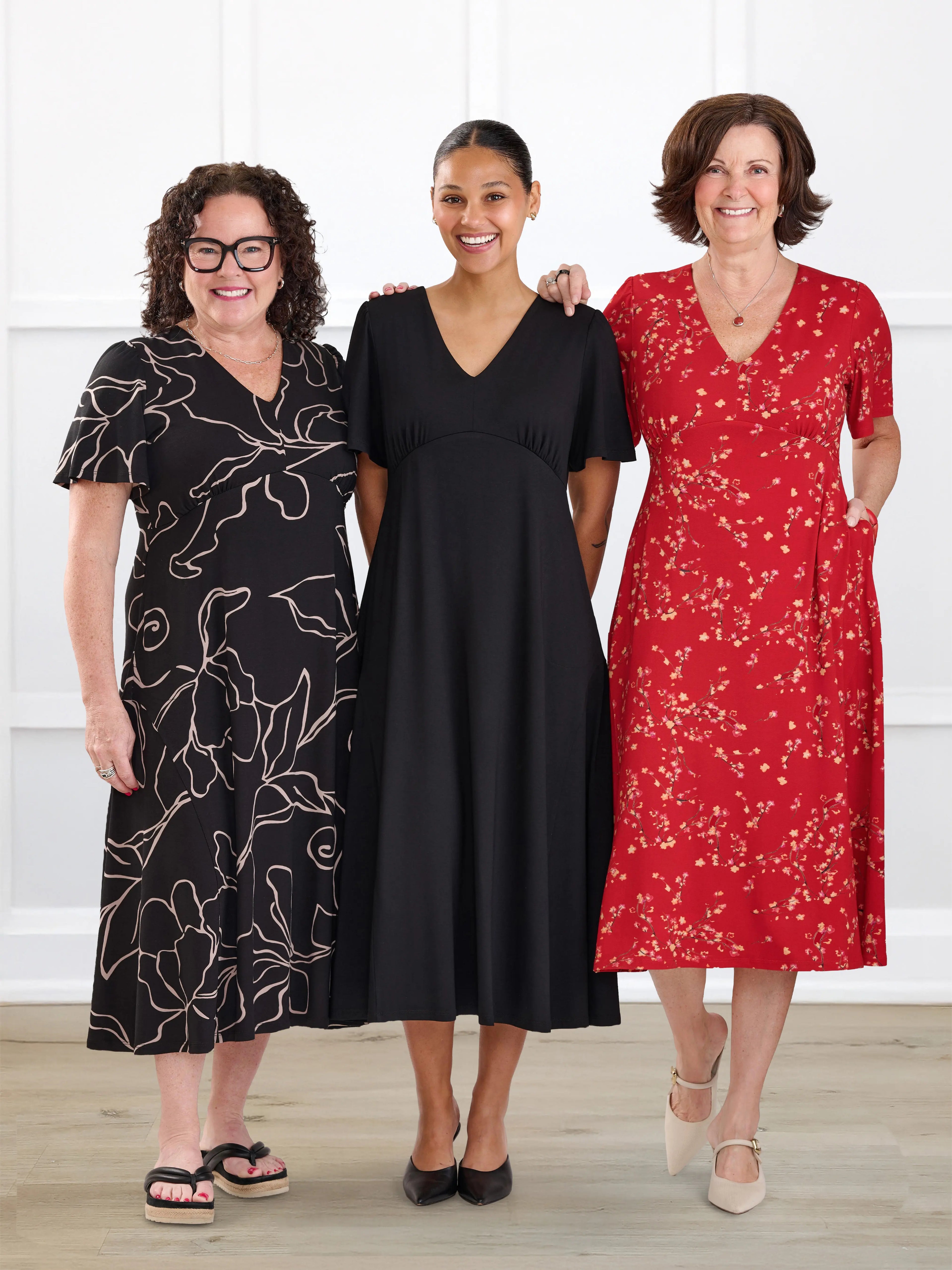 Three women wearing different dresses standing together against a white background
